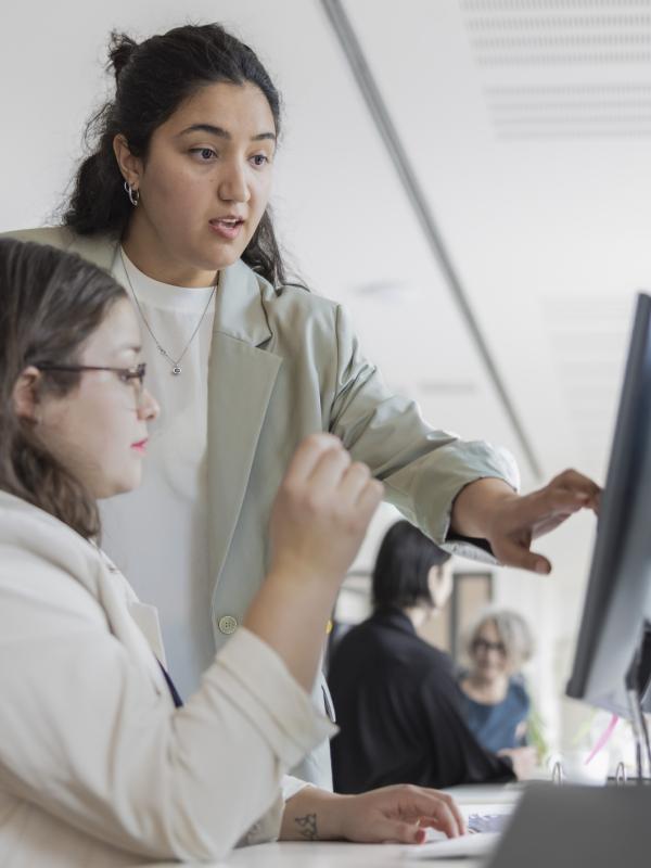 Eine Frau erklärt einer Mitarbeiterin etwas auf ihrem Computer