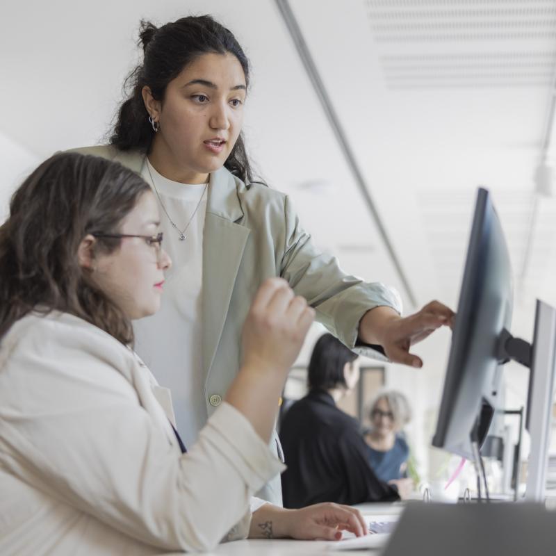 Eine Frau erklärt einer Mitarbeiterin etwas auf ihrem Computer