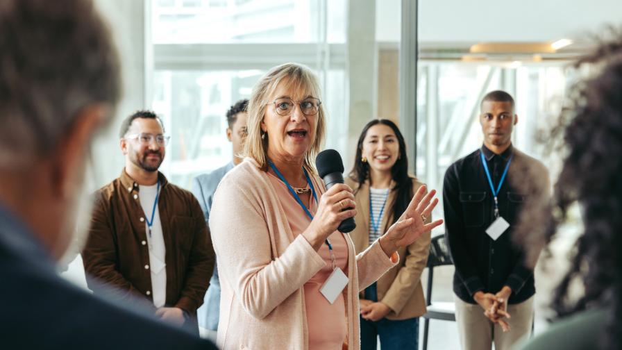 Frau mittleren Alters spricht inmitten einer Gruppe von Menschen in einem Workshop